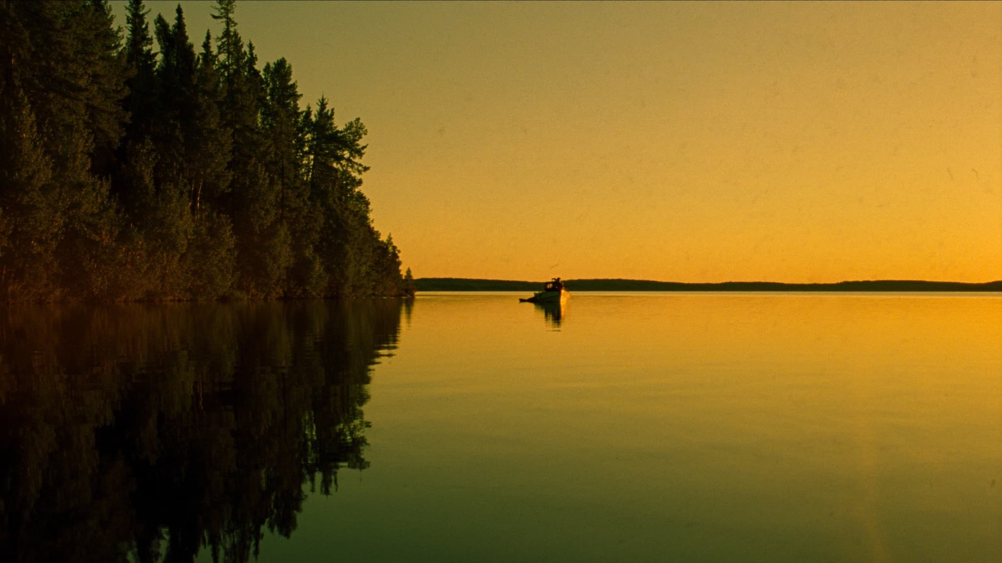 A calm northern Minnesota lake at golden hour, pines reflected in still water, a lone boat sitting level out toward the sunset